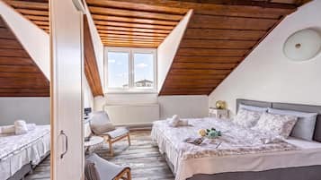 A cozy attic bedroom with a sloped ceiling, two beds, a chair, and a window with a view.