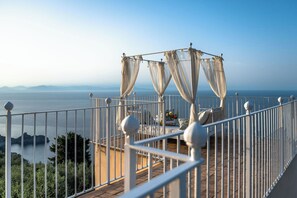 Un balcón con barandilla de metal blanco, un toldo y vista al mar.