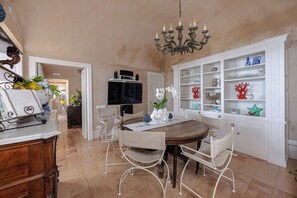 A dining area with a wooden table, white chairs, a chandelier, and a white cabinet with glassware. - Villa in San Michele with 5 bedrooms sleeps 10 (San Michele)
