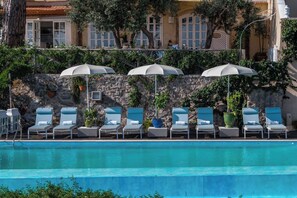 A poolside area with lounge chairs and umbrellas, a stone wall, and a building with windows in the background. - Villa in San Michele with 5 bedrooms sleeps 10 (San Michele)