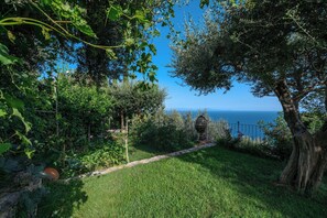 Un jardín con vista al mar, un sendero de piedra y una maceta rústica.