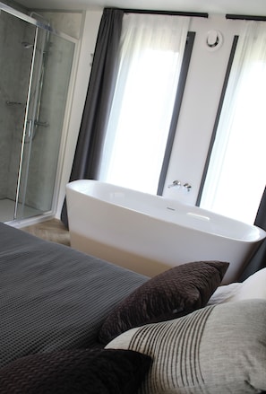 A modern bathroom with a freestanding bathtub, a glass shower enclosure, and a large window with curtains. - EuroParcs Ossiacher See (Ossiach)
