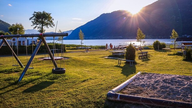 A lakeside park with swings, picnic tables, and a view of the lake and mountains. - EuroParcs Ossiacher See (Ossiach)