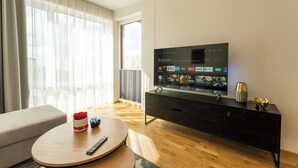 A modern living room with a flat-screen TV, a sofa, a coffee table, and a black entertainment unit. - CITYGATE SUNSET BALCONY (Tartu)