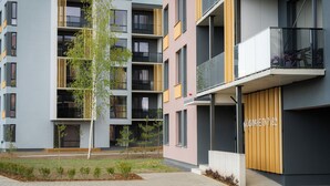 A multi-story residential building with balconies, a small garden area, and a parking lot. - CITYGATE SUNSET BALCONY (Tartu)