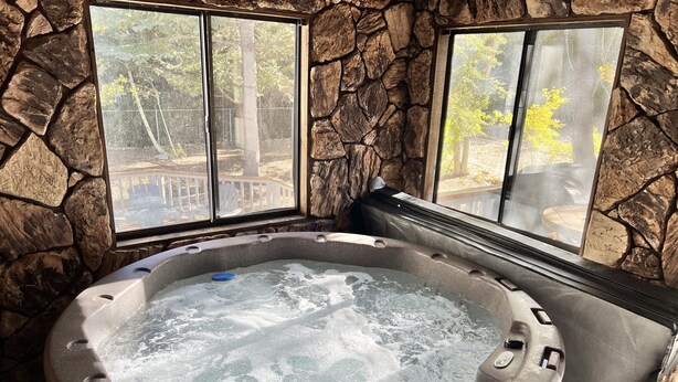 A hot tub with stone walls and windows overlooking a deck. - 1 Mile to Summit or Village*Spa/Arcades/Pool Table (Big Bear Lake)