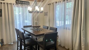 A dining area with a wooden table, six chairs, a chandelier, and a sign that reads "Meals & memories are made here." - 1 Mile to Summit or Village*Spa/Arcades/Pool Table (Big Bear Lake)