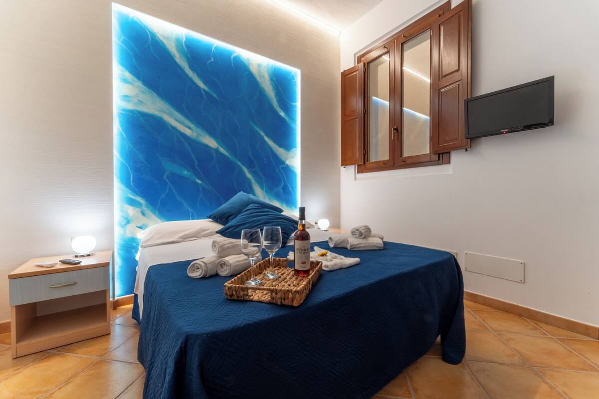 A hotel room with a bed, a nightstand, a TV, and a wall with a blue abstract design.