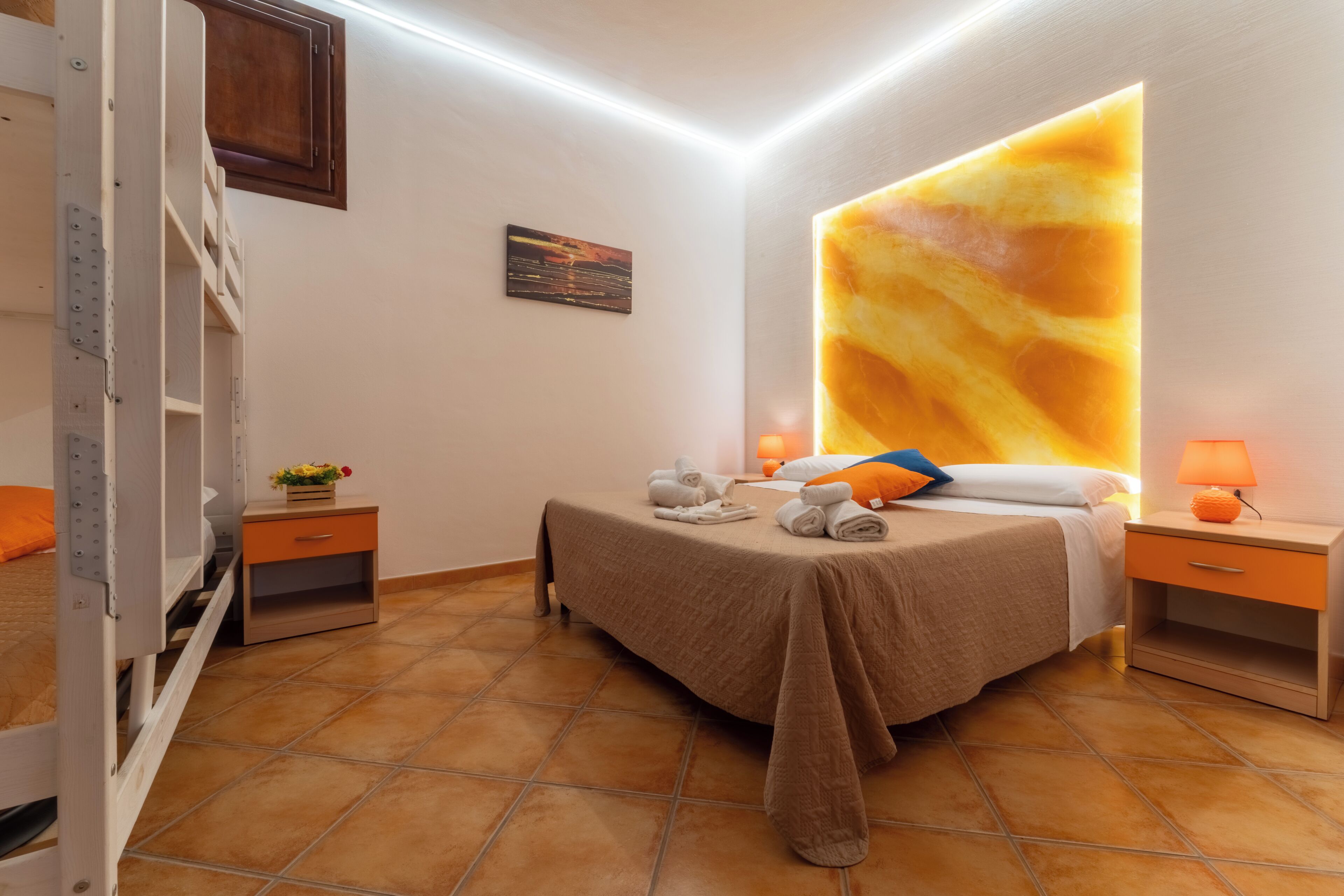 A bedroom with a bed, nightstands, a wall-mounted lamp, and a tiled floor.