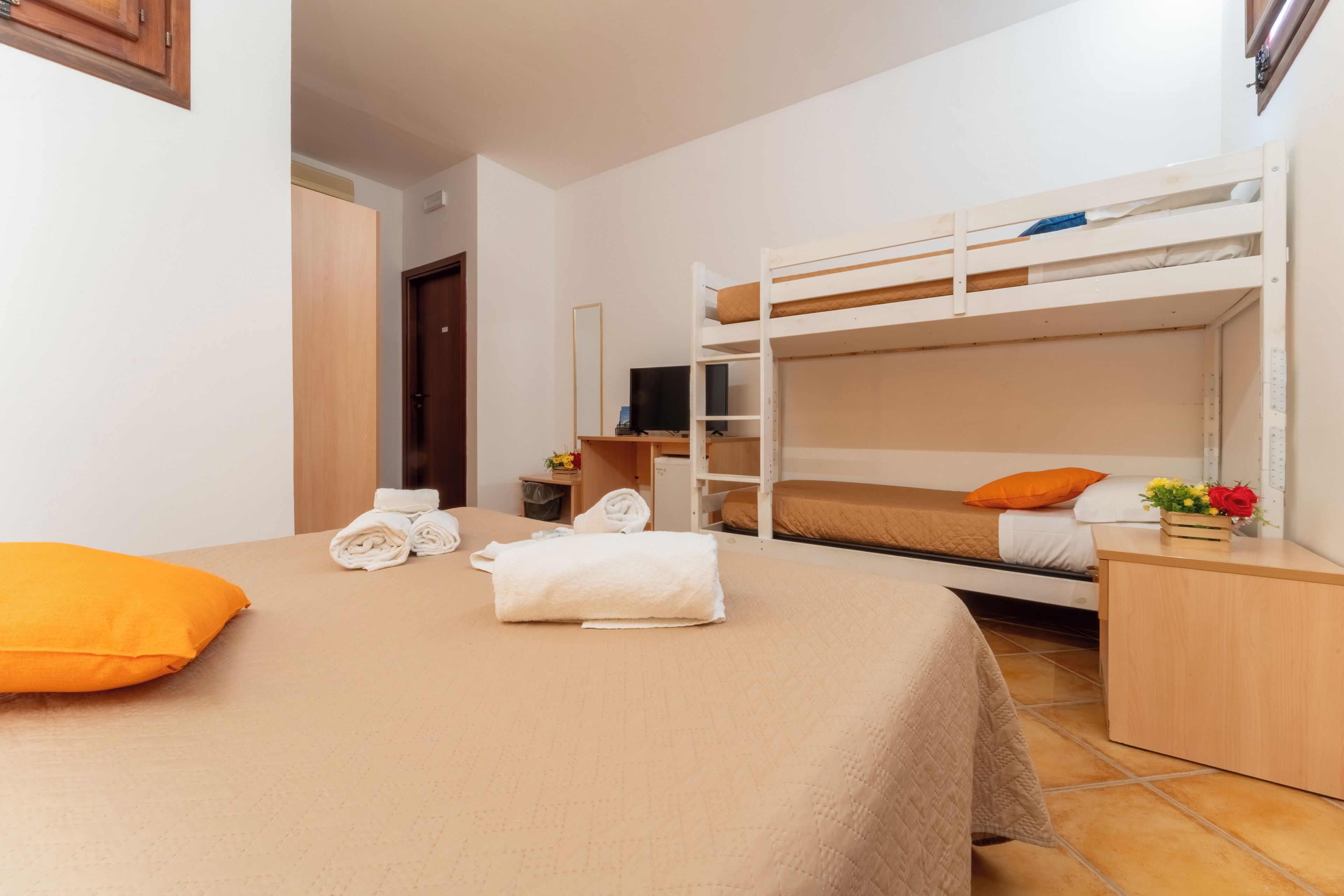 A bunk bed room with a desk, a mirror, and a TV.