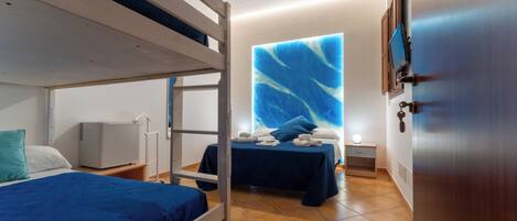 A room with bunk beds, a desk, a chair, a small table, a wall-mounted TV, and a door.