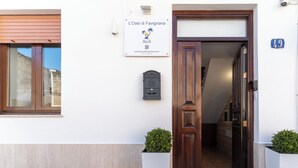 A building entrance with a wooden door, a sign above it, and two potted plants. - L'Oasi di Favignana Room and Charme (Favignana)