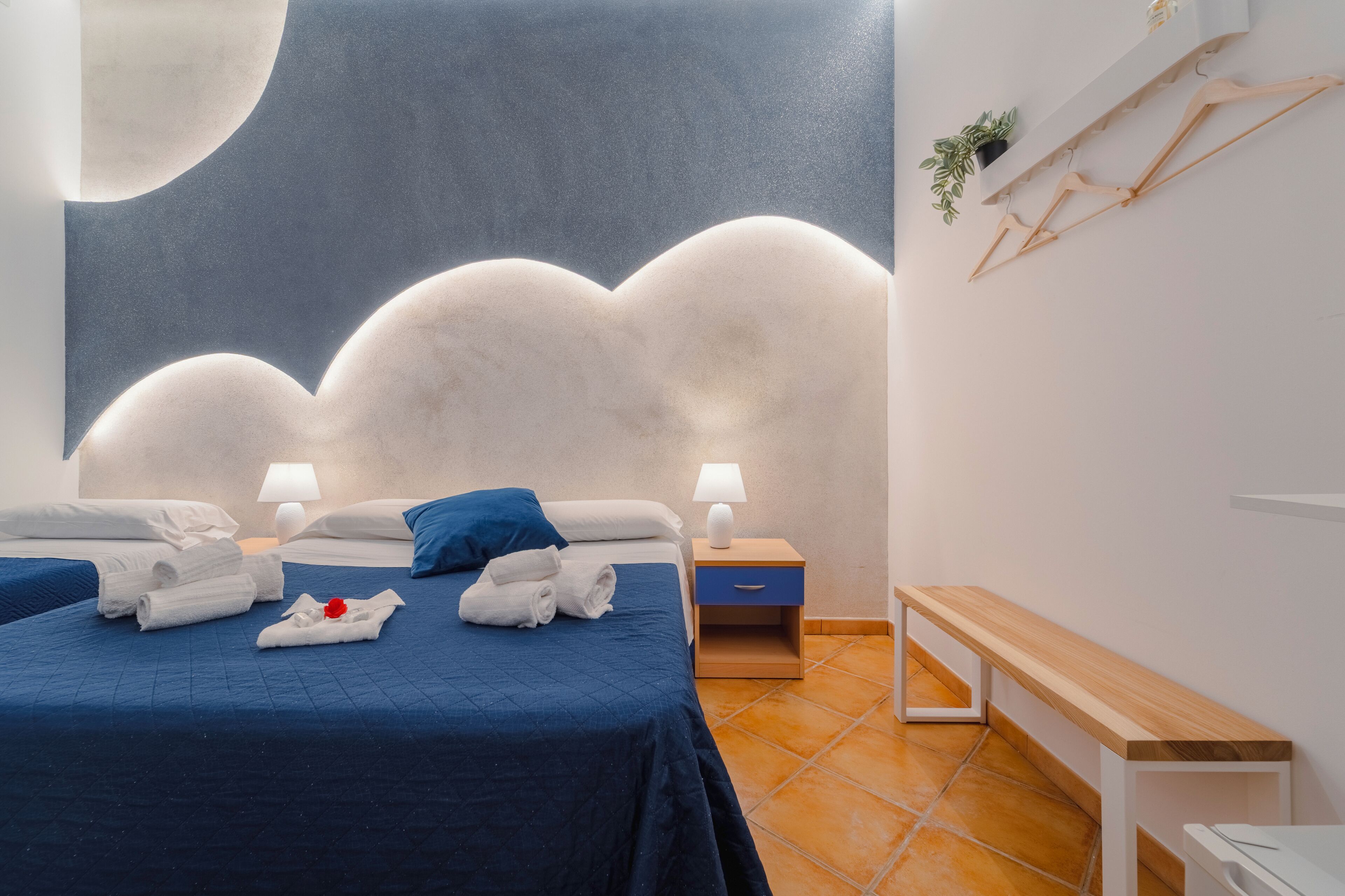 A hotel room with a bed, two bedside tables, a bench, and a wall with a crescent moon design.