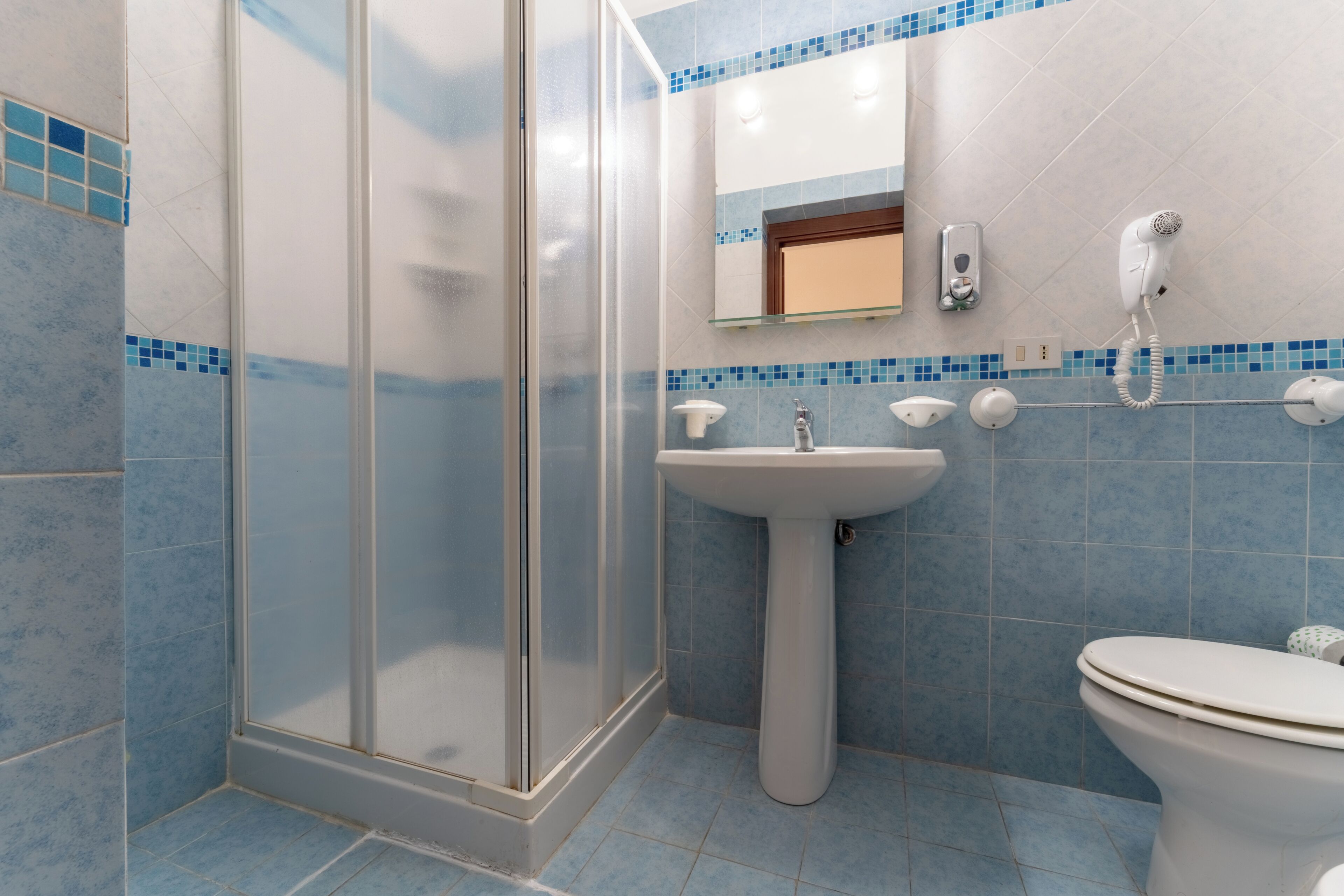 Ein Badezimmer mit Duschkabine aus Glas, einem Standwaschbecken, einer Toilette und einem Spiegel über dem Waschbecken.