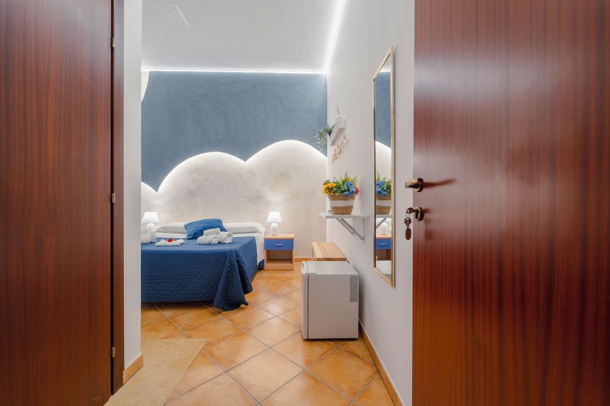 A bedroom with a bed, bedside table, lamp, and a small white appliance.
