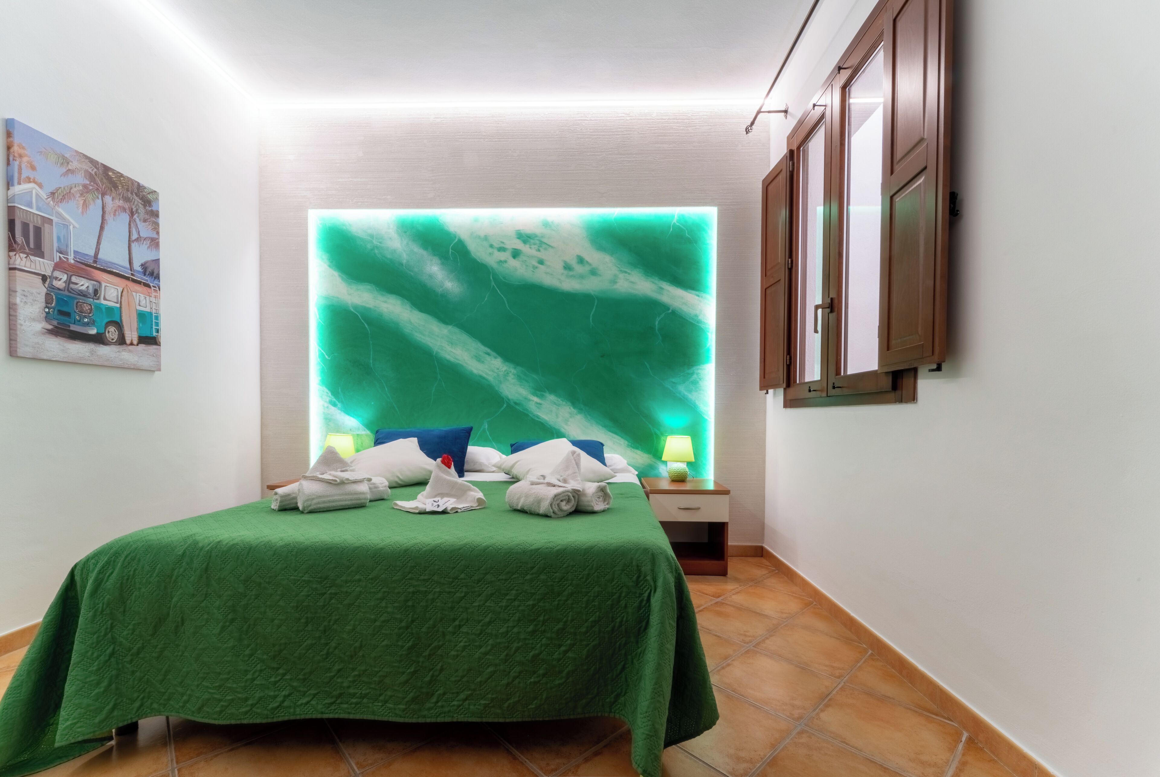 A hotel room with a bed, a wall-mounted TV, a nightstand with a lamp, and a painting on the wall.