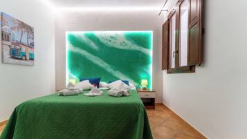 A hotel room with a bed, a wall-mounted TV, a nightstand with a lamp, and a painting on the wall.