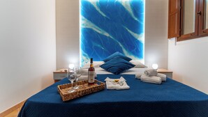 A neatly made bed with a blue bedspread, a bottle of wine, glasses, and towels on a bedside table. - L'Oasi di Favignana Room and Charme (Favignana)