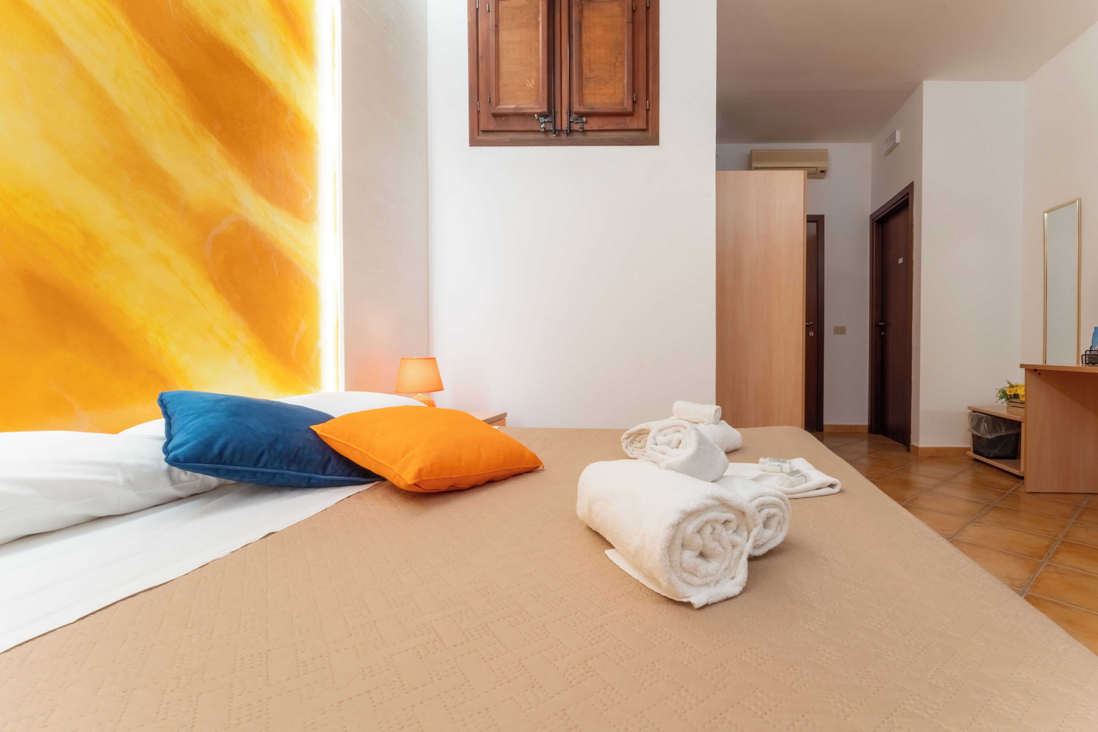 Une chambre d’hôtel avec un lit, des oreillers, une lampe, des serviettes, une armoire en bois et un miroir.