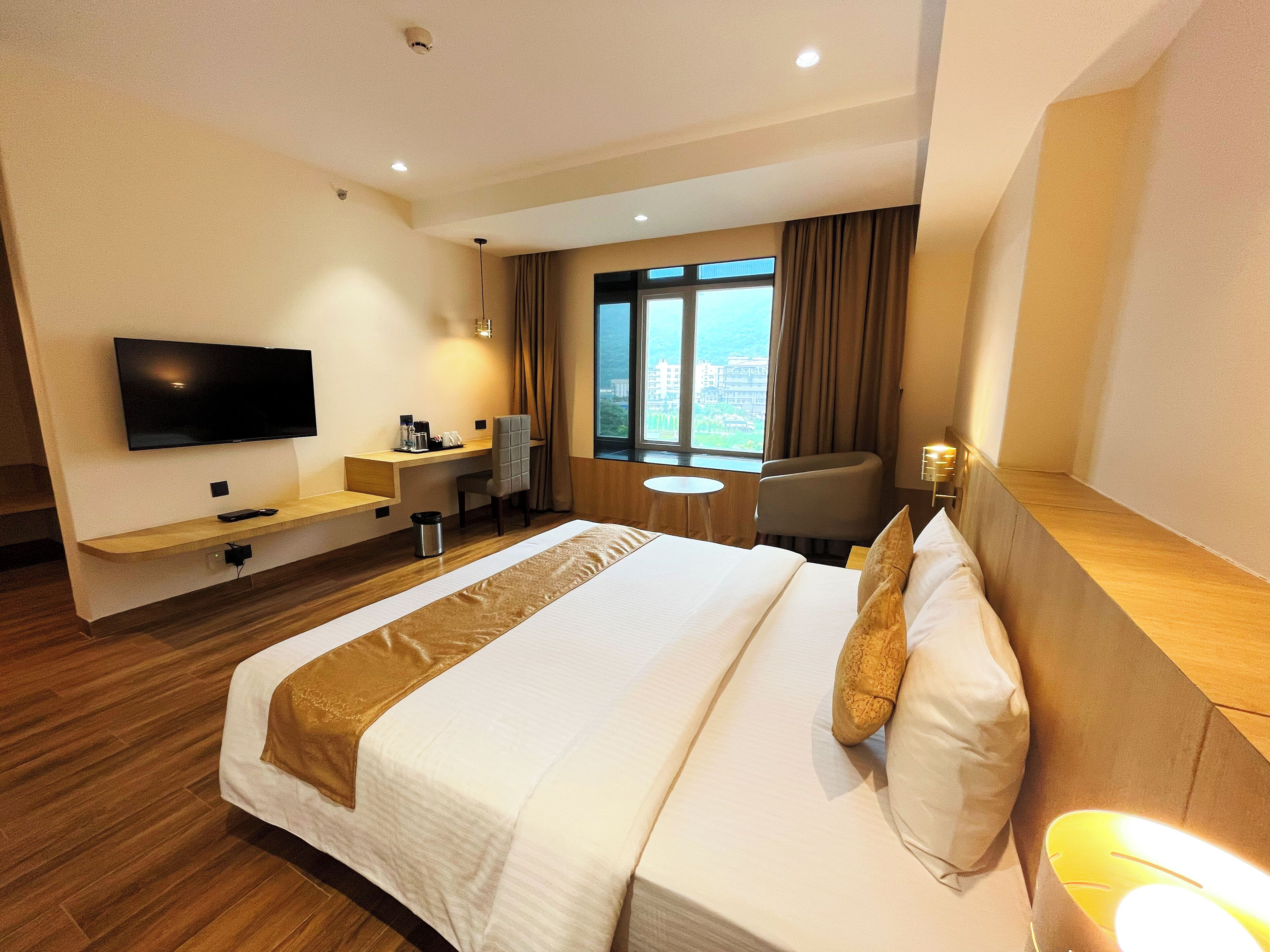 A hotel room with a bed, a desk, a TV, and a window with a view.
