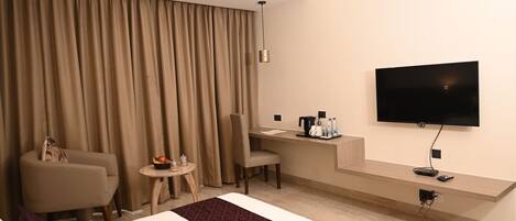 Habitación de hotel con cama, escritorio, silla, televisor y ventana con cortinas.