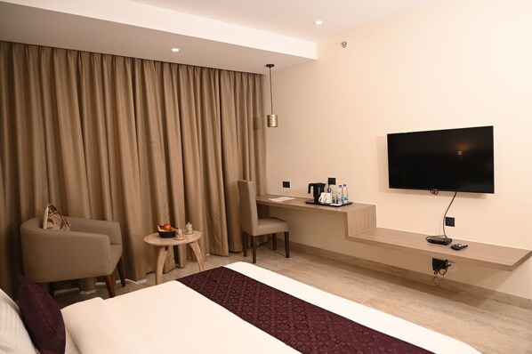 A hotel room with a bed, a desk, a chair, a TV, and a window with curtains.
