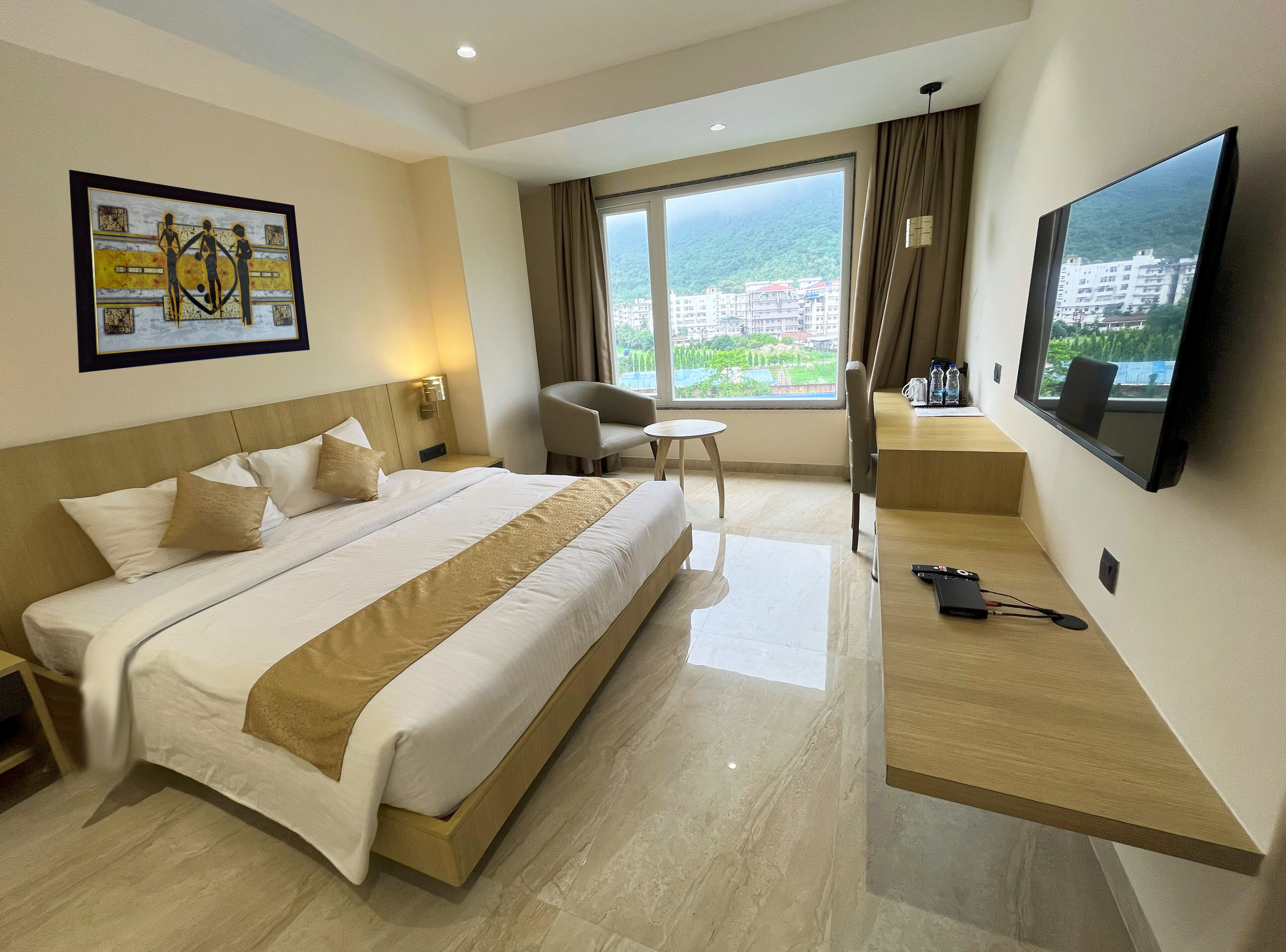 A hotel room with a large bed, a desk, a chair, a TV, and a window with a view of buildings and greenery.