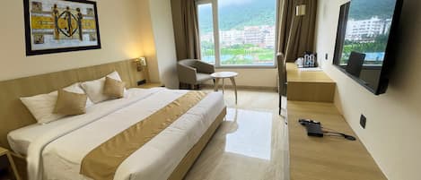 A hotel room with a large bed, a desk, a chair, a TV, and a window with a view of buildings and greenery.