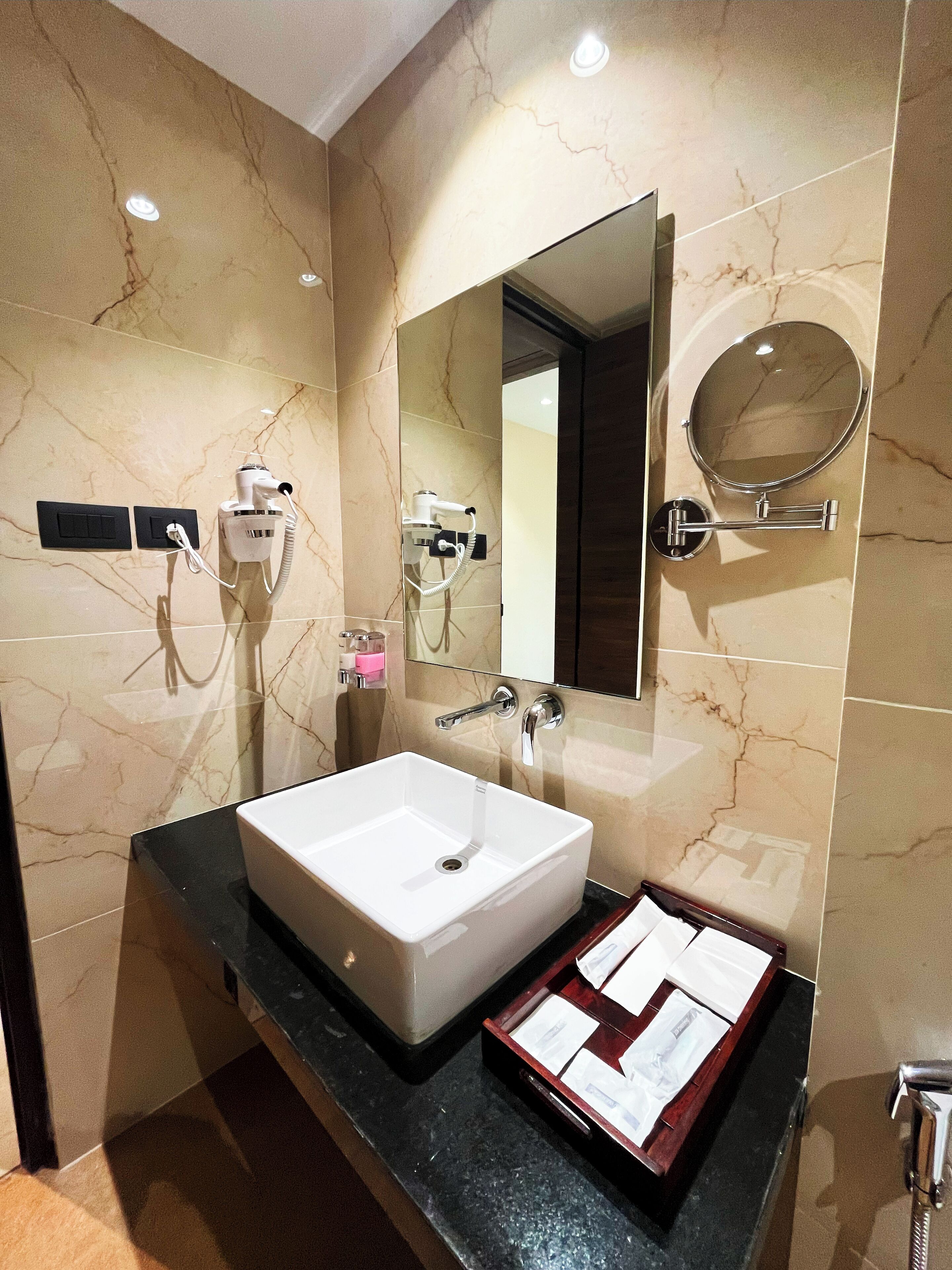 A bathroom with a marble wall, a white sink, a mirror, and a hairdryer.