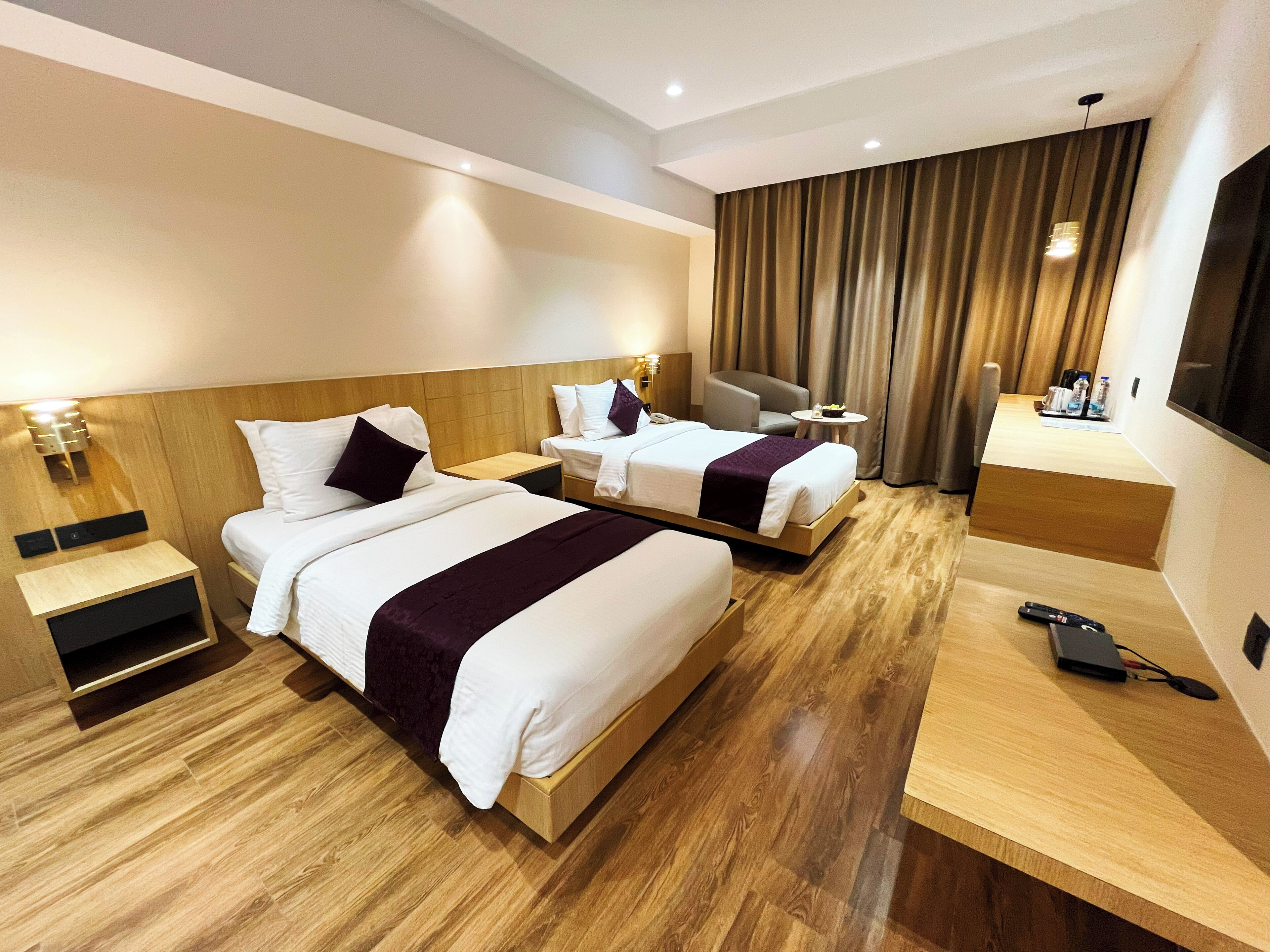 Ein Hotelzimmer mit zwei Betten, einem Schreibtisch, einem Sessel und einem Fernseher.
