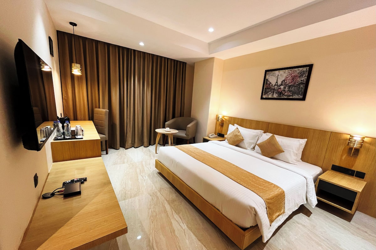 A hotel room with a bed, bedside tables, a desk, a chair, a TV, and a curtain.