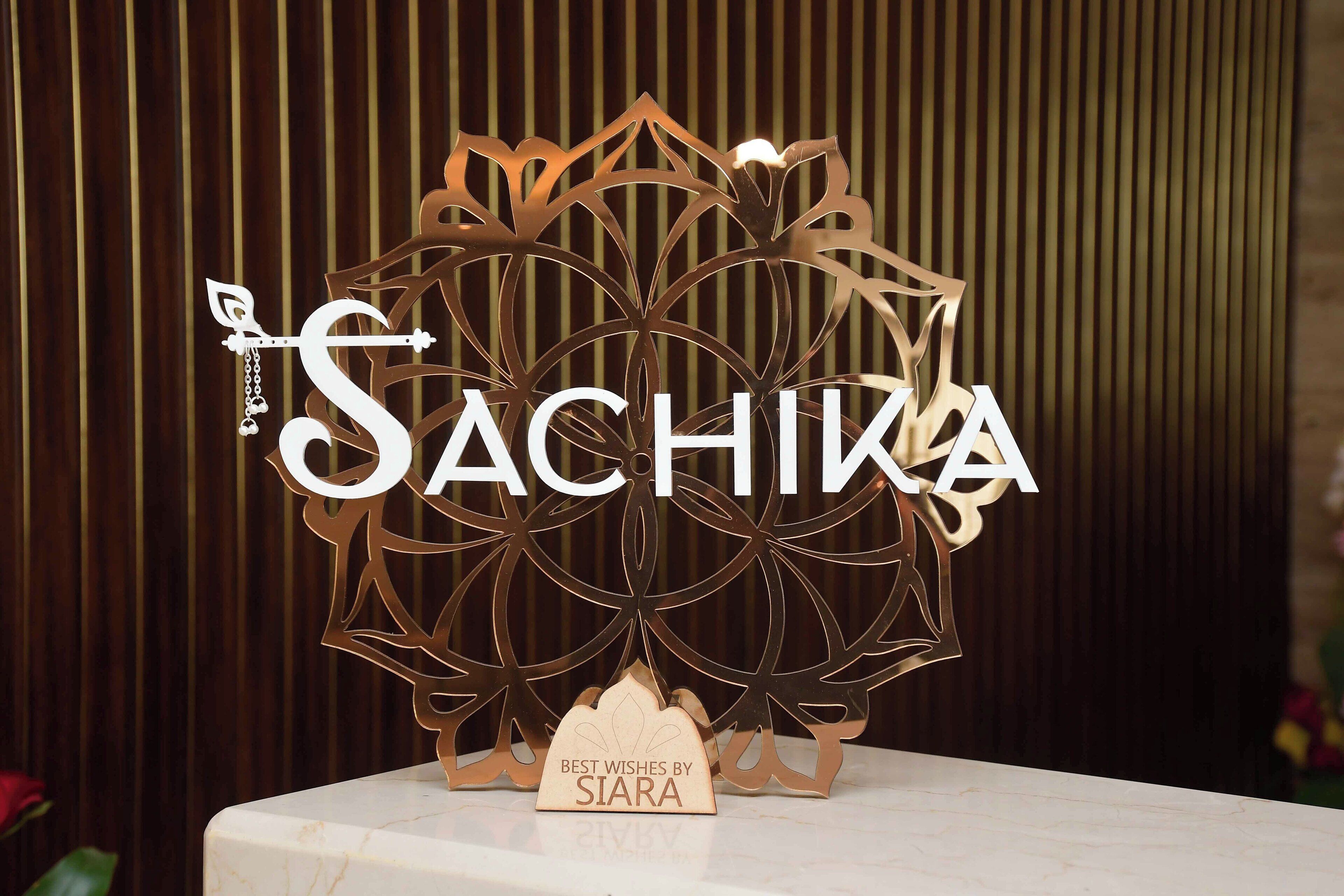 A decorative metal sign with the name "SACHIYA" and a smaller sign below it stating "BEST WISHES BY SIARA".