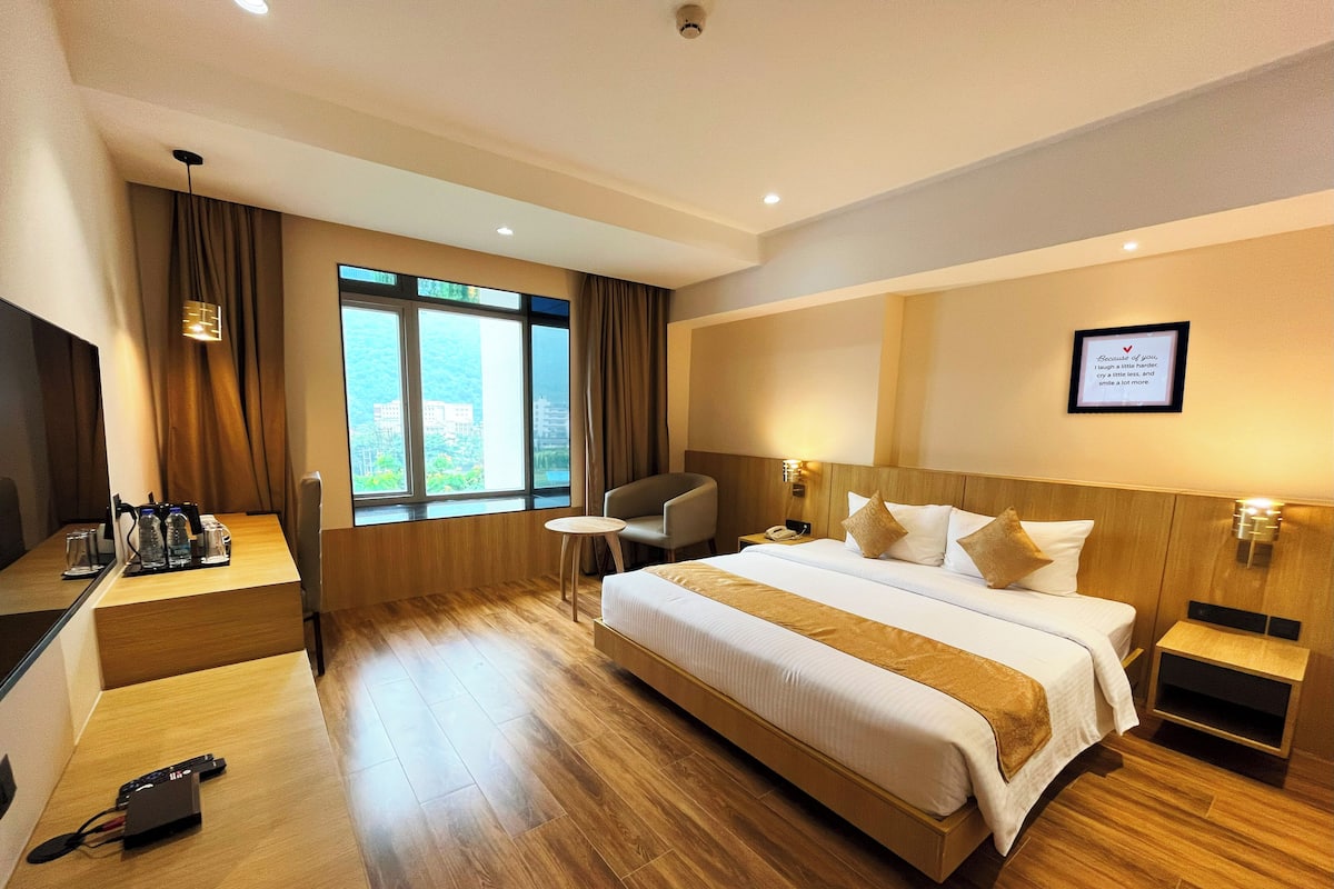 A hotel room with a large bed, a desk with a chair, a small table, and a TV.