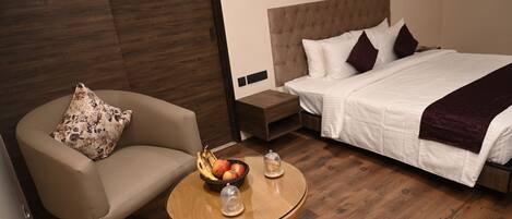 A hotel room with a bed, a chair, a small table with fruit, and a nightstand.