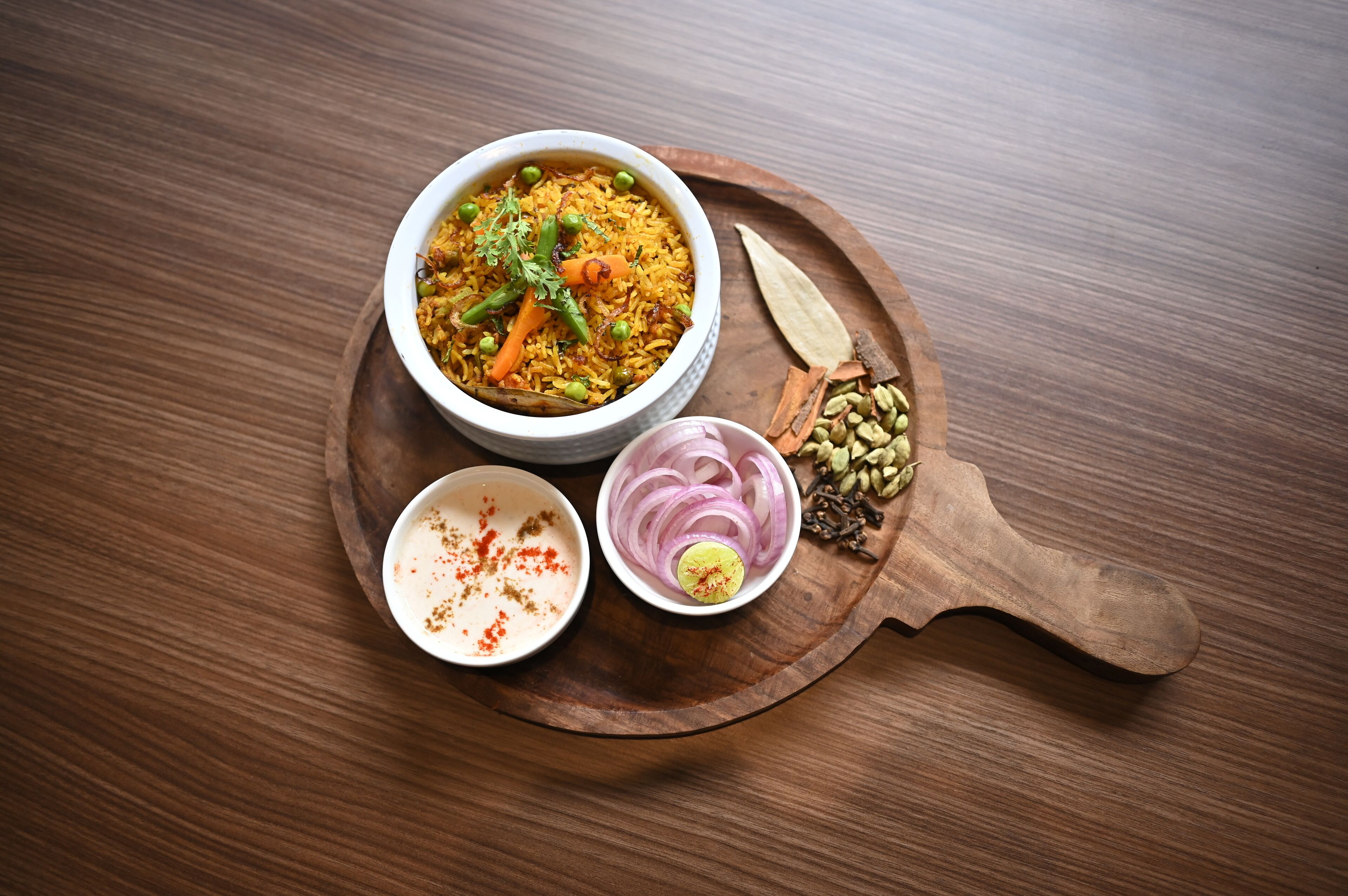 A bowl of rice with vegetables and a small bowl of sauce on a wooden board.
