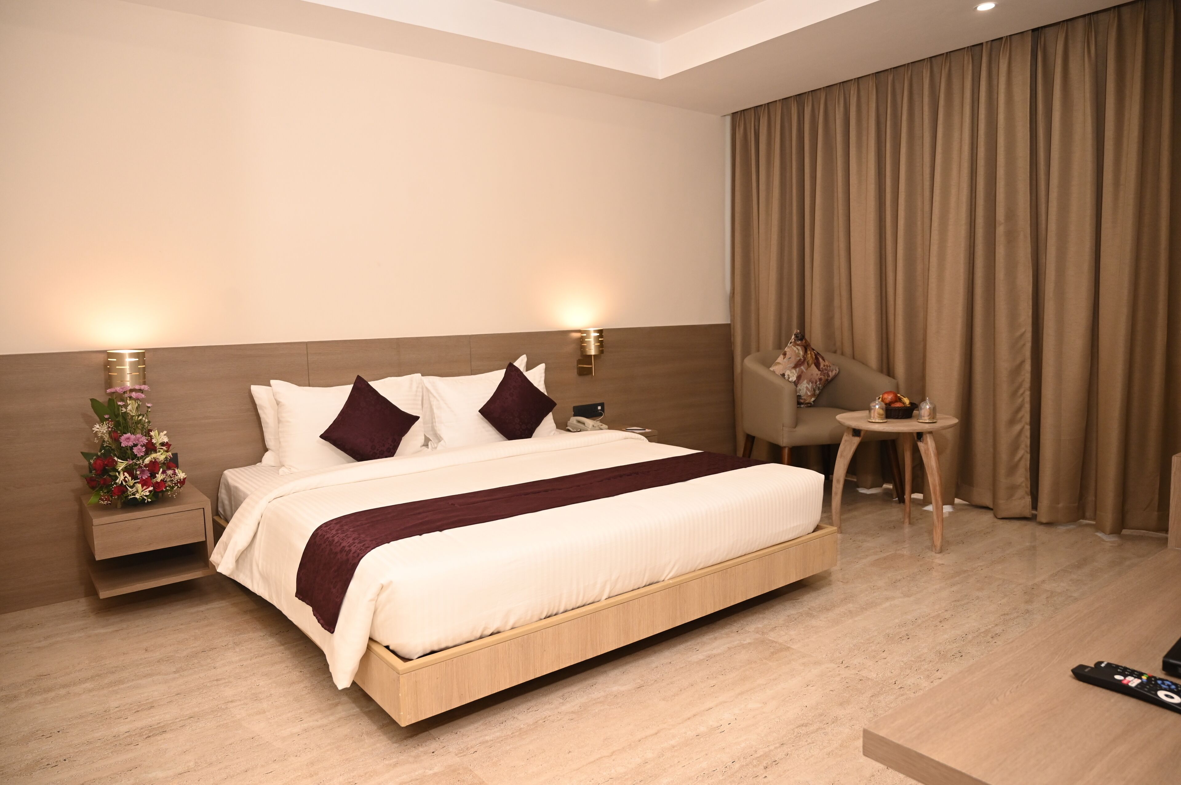 A hotel room with a large bed, bedside tables, a small round table with a chair, and a curtain.