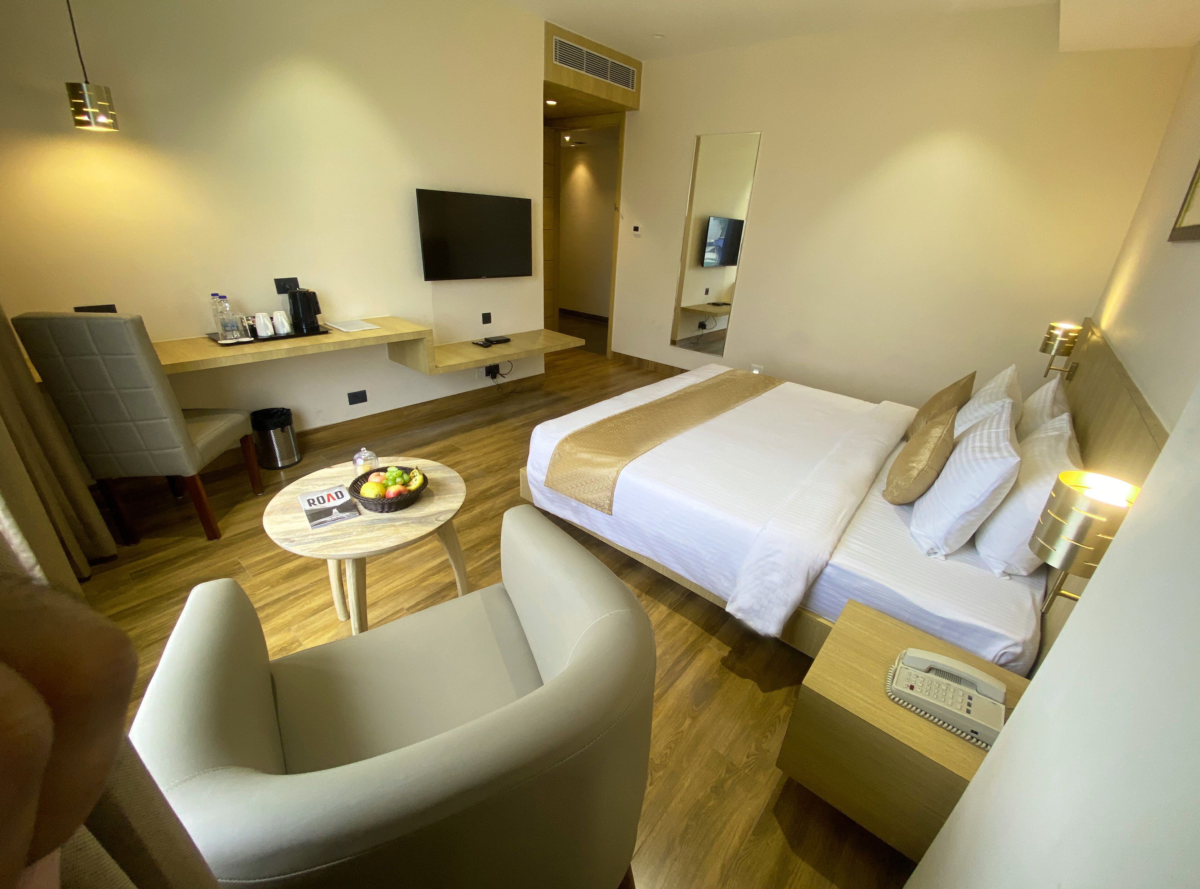 Habitación de hotel con cama, escritorio, silla, mesita con frutero, televisor y teléfono sobre la mesita de noche.