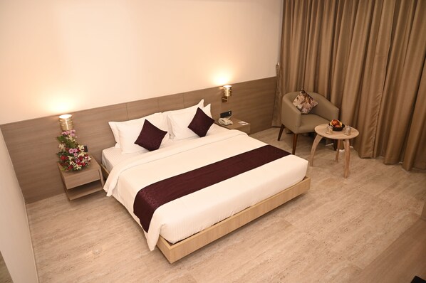 Una habitación de hotel con una cama grande, mesitas de noche, una silla y una pequeña mesa con lámpara.