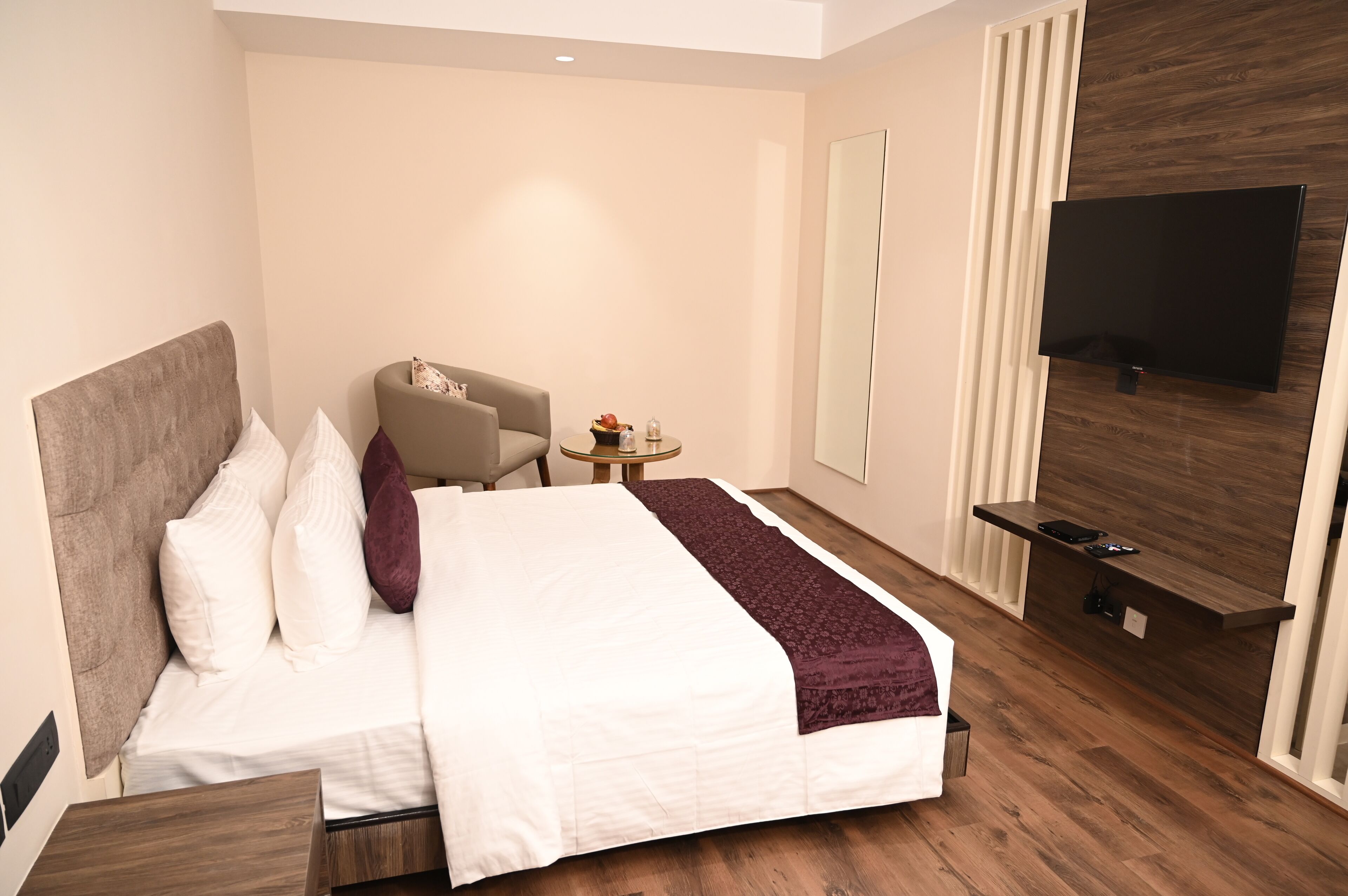 A modern hotel room with a large bed, a TV mounted on the wall, a small round table, and a chair.