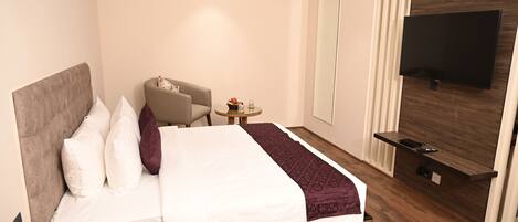 A modern hotel room with a large bed, a TV mounted on the wall, a small round table, and a chair.