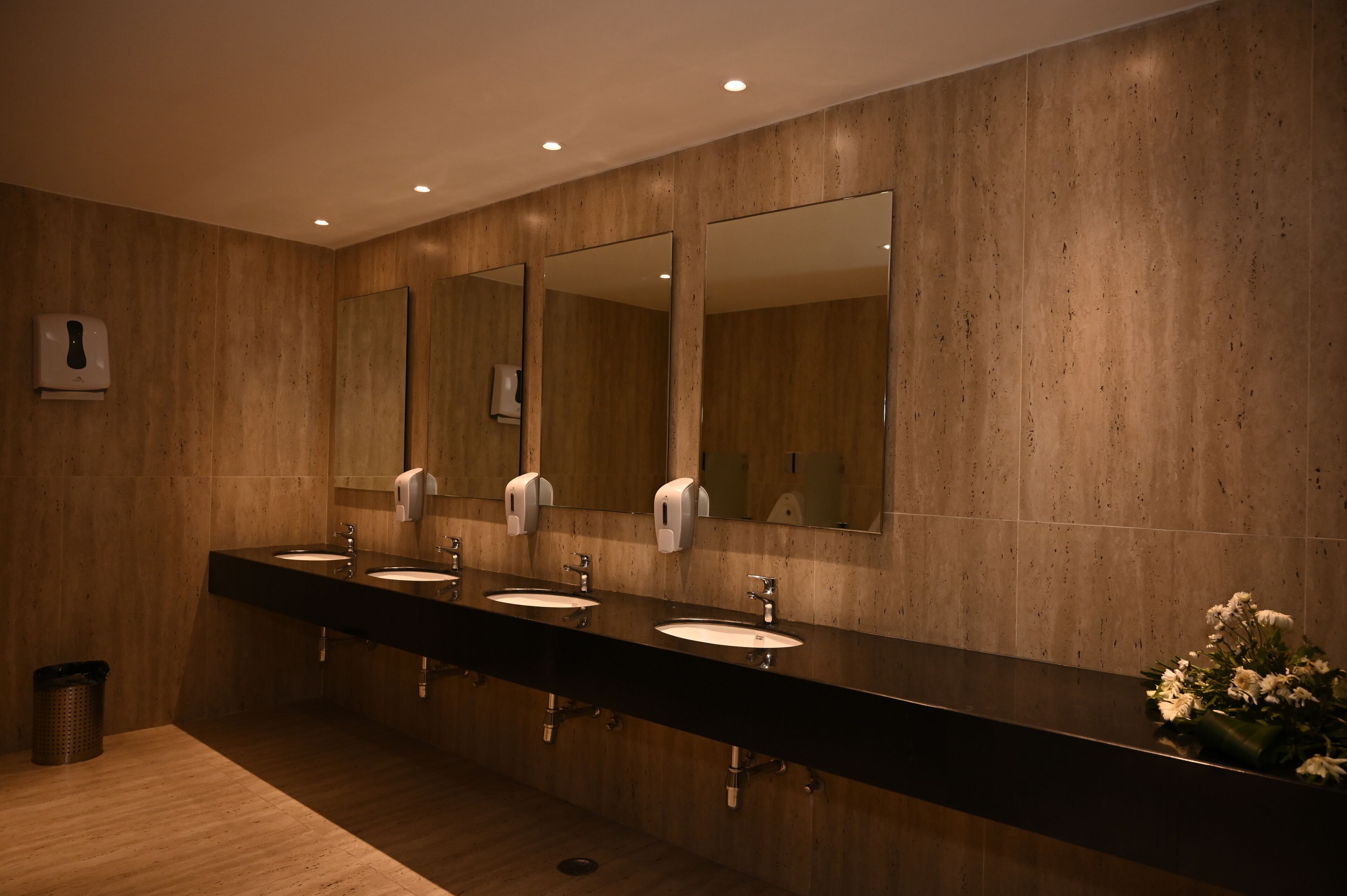 Une salle de bain moderne avec trois lavabos, de grands miroirs et des sèche-mains.