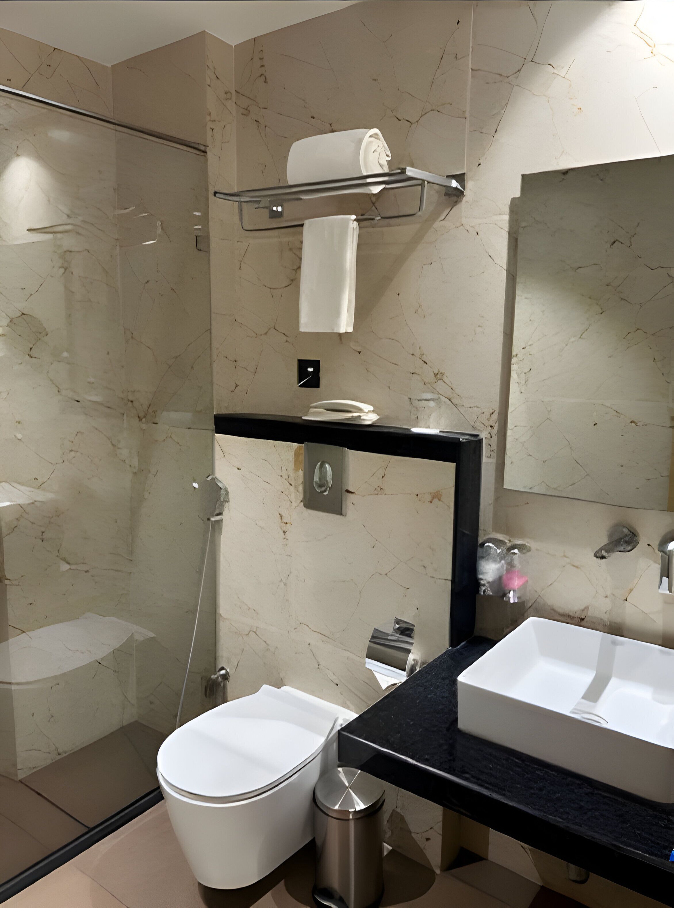Un baño moderno con cabina de ducha de vidrio, inodoro blanco, lavabo con encimera negra y pared de mármol.