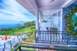 Ein Balkon mit Blick auf eine üppige Landschaft, ein weißer Zaun und ein roter Tisch mit Stühlen.