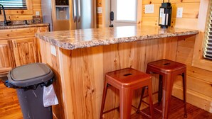 Uma cozinha com paredes de madeira, bancada de granito e eletrodomésticos de aço inoxidável, além de dois banquetes.