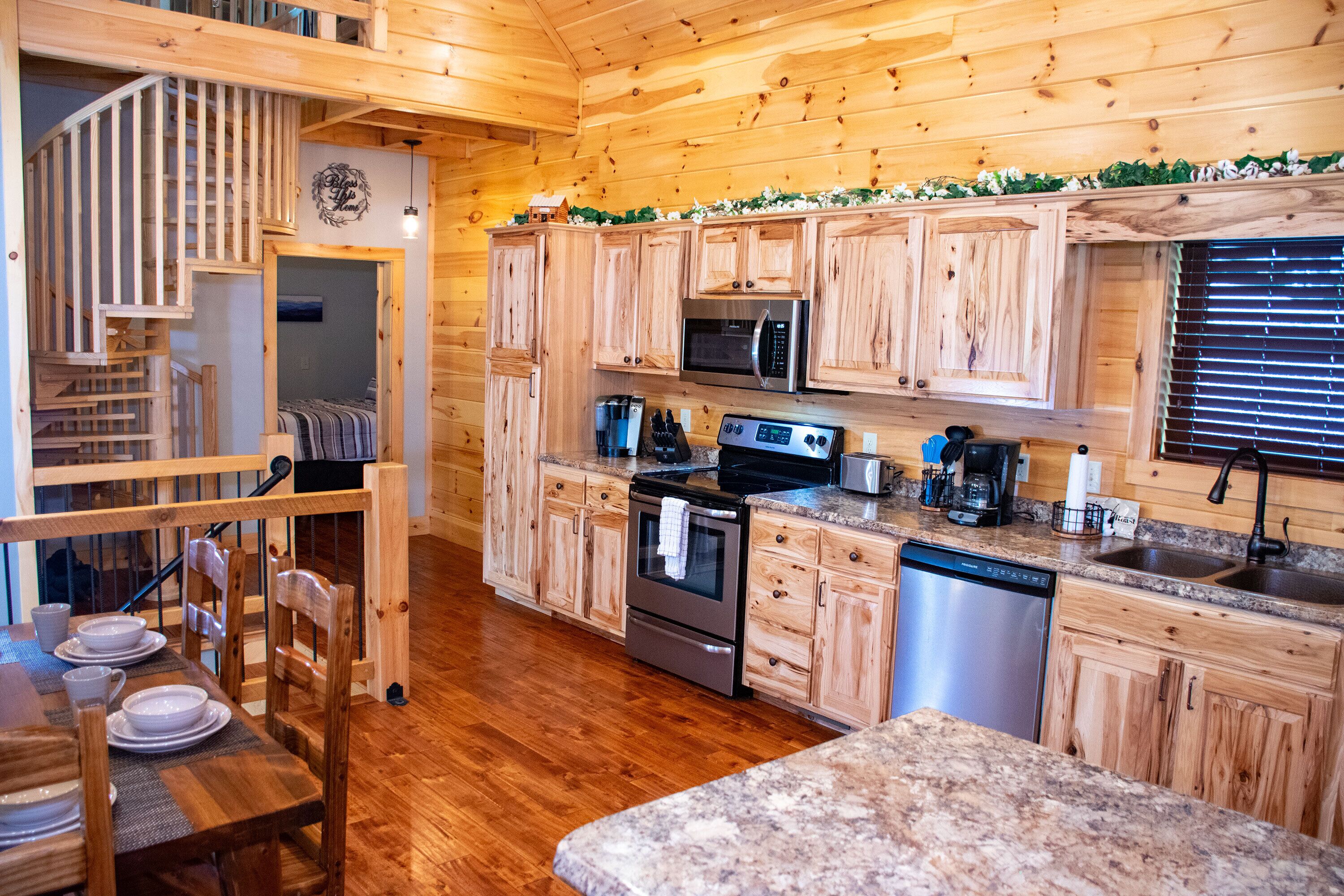 A wooden cabin kitchen with a wooden staircase, stainless steel appliances, and a granite countertop.