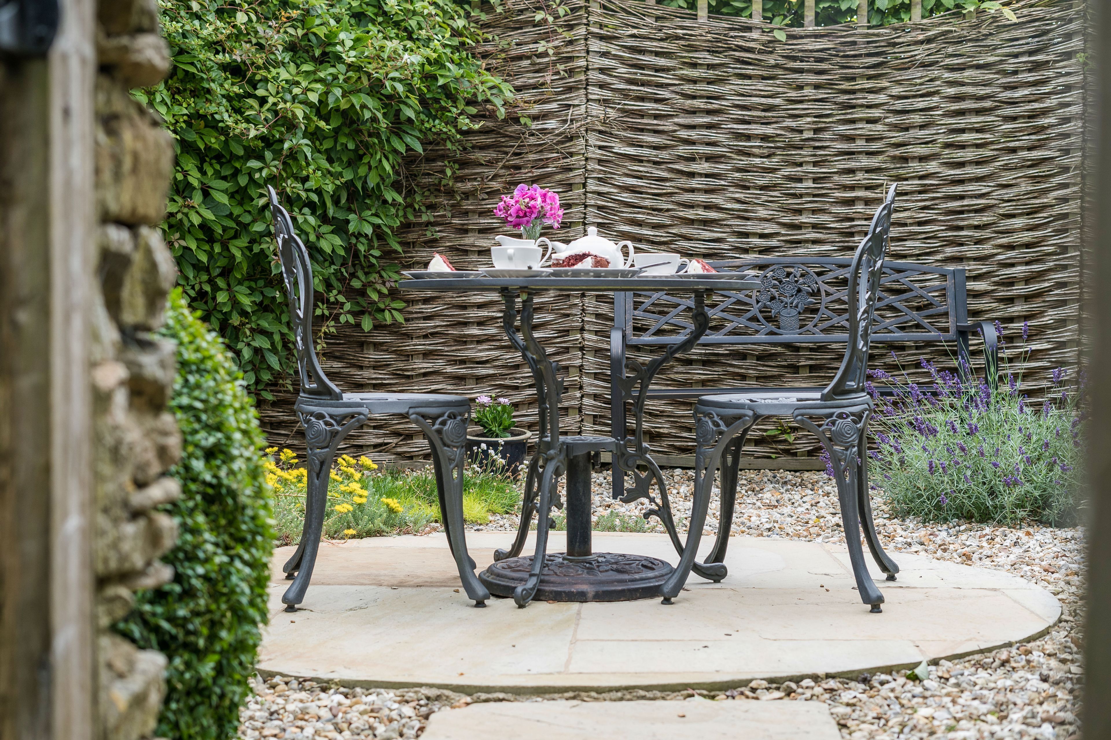 A round table with four chairs, a wicker backdrop, and a stone wall.