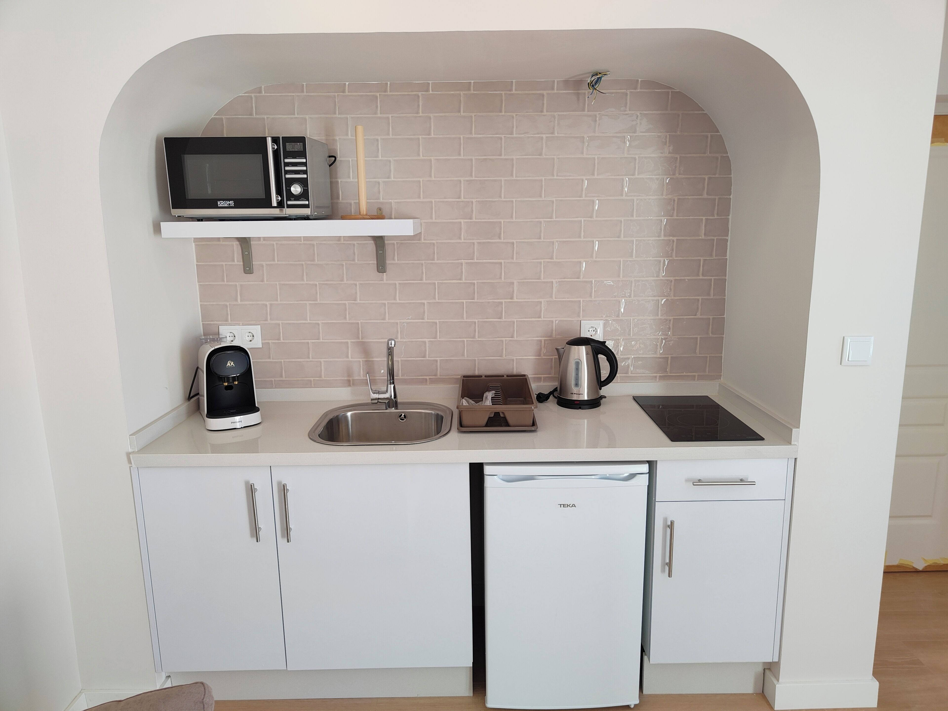 Een kleine keuken met een magnetron, waterkoker, koffiezetapparaat en vaatwasser.