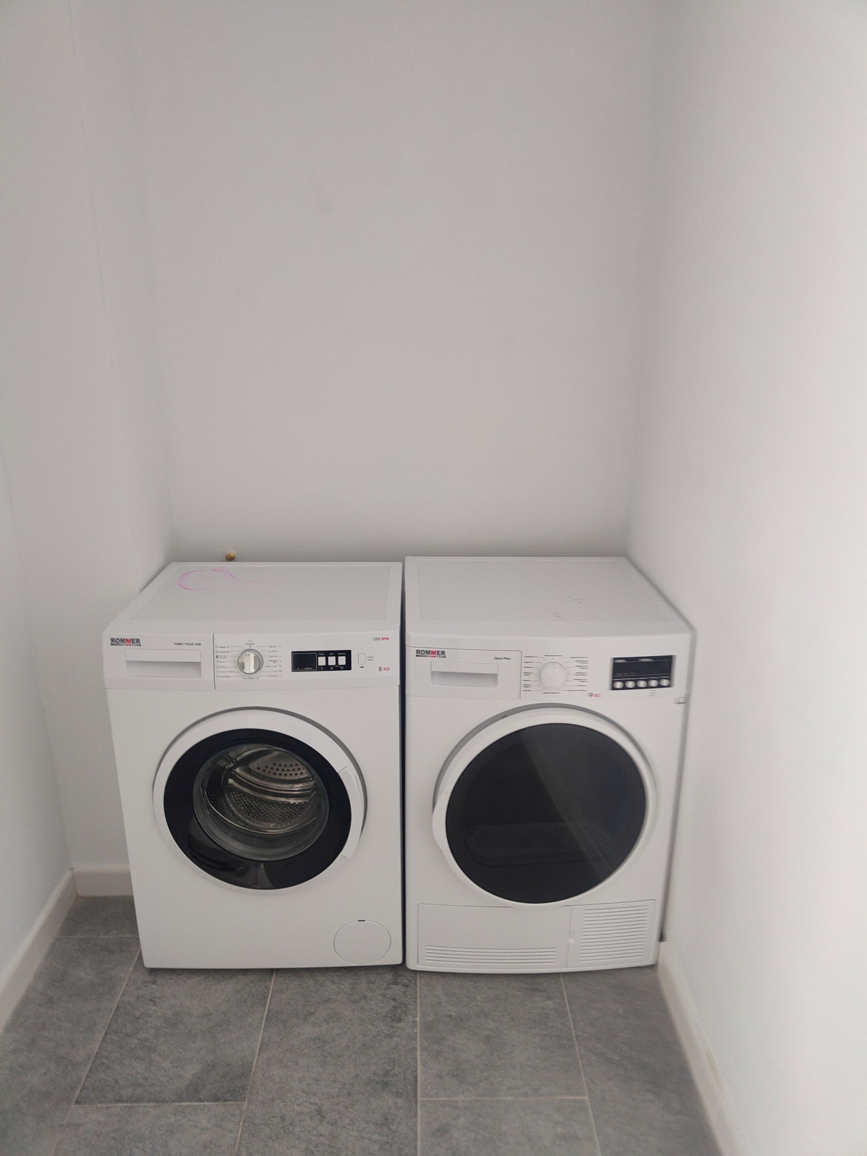 Two white front-loading washing machines in a corner with a tiled floor.