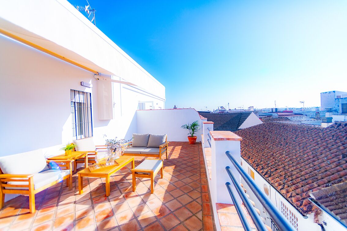 Terraço no telhado com um edifício branco, piso de azulejos, mobiliário de exterior e vista para a paisagem urbana.