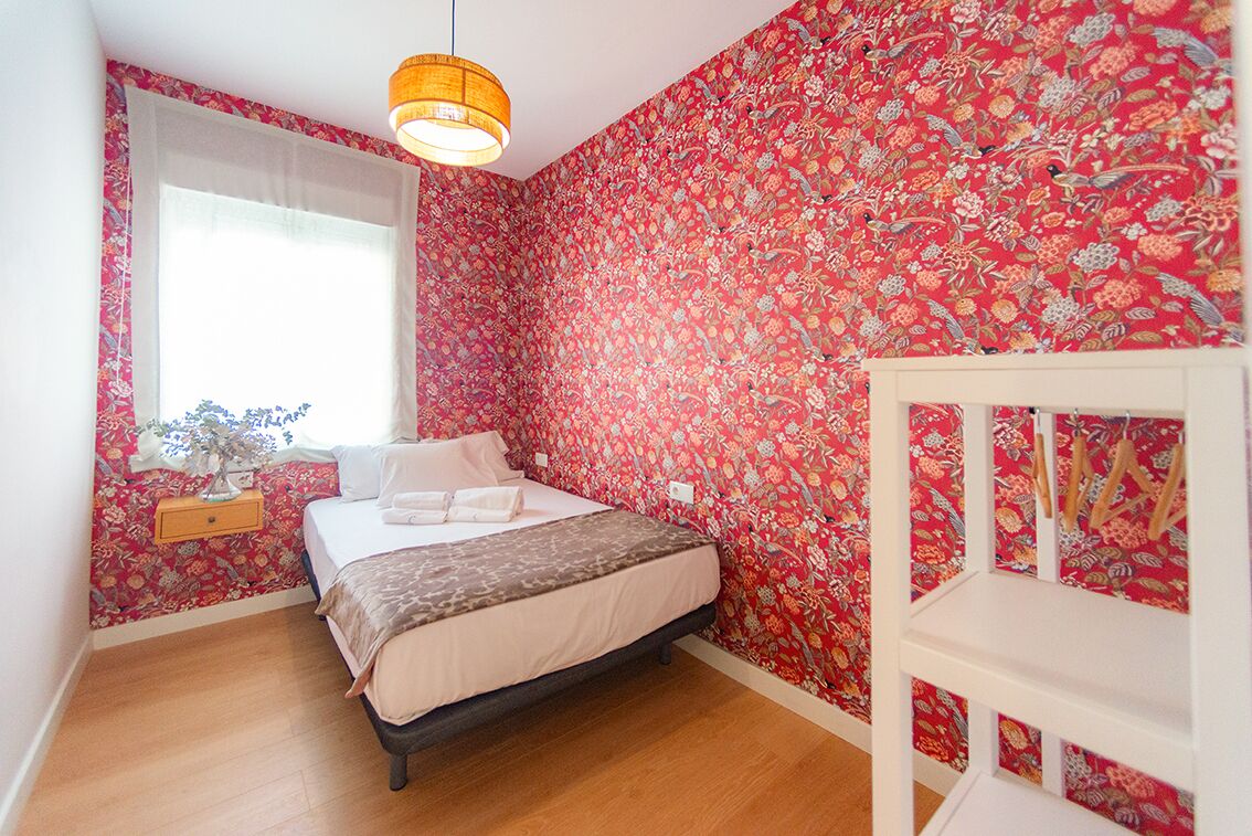 Un dormitorio con cama, mesita de noche, ventana y mueble de pared.